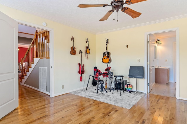 interior space featuring a ceiling fan, visible vents, a textured ceiling, crown molding, and light wood-type flooring