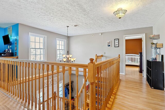 hallway with wood finished floors, baseboards, an inviting chandelier, a textured ceiling, and an upstairs landing