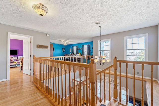 corridor with visible vents, baseboards, an upstairs landing, an inviting chandelier, and wood finished floors