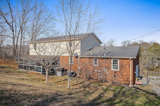back of property featuring cooling unit, a yard, a sunroom, brick siding, and metal roof
