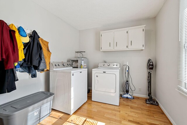 washroom featuring washing machine and clothes dryer, light wood finished floors, baseboards, water heater, and cabinet space