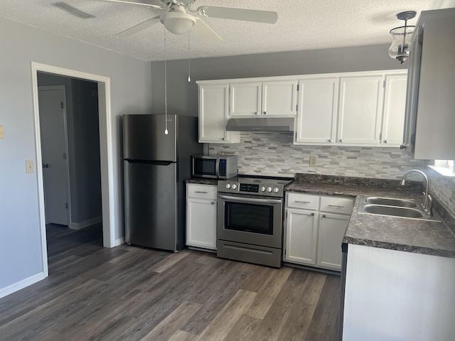 kitchen featuring under cabinet range hood, a sink, dark countertops, white cabinetry, and appliances with stainless steel finishes