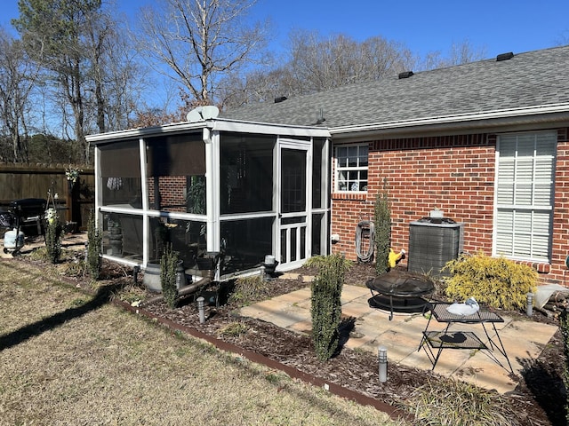 back of property featuring a sunroom, an outdoor fire pit, a shingled roof, and a patio area