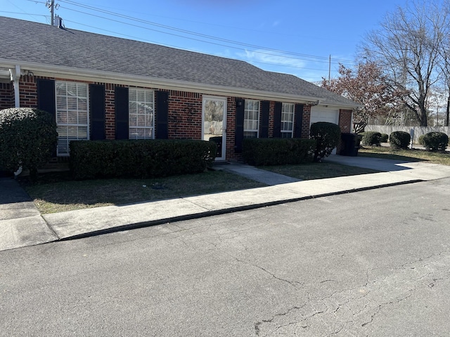 ranch-style house with an attached garage, fence, brick siding, and a shingled roof