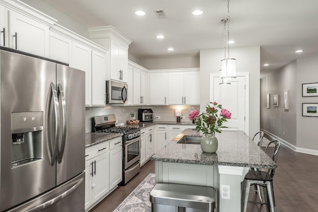 kitchen featuring visible vents, backsplash, stainless steel appliances, a breakfast bar area, and white cabinets