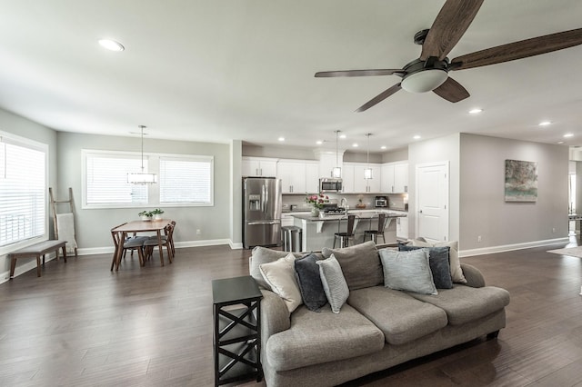 living room featuring ceiling fan with notable chandelier, dark wood-type flooring, recessed lighting, and baseboards