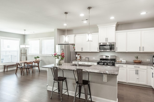 kitchen featuring an island with sink, a sink, backsplash, white cabinetry, and appliances with stainless steel finishes