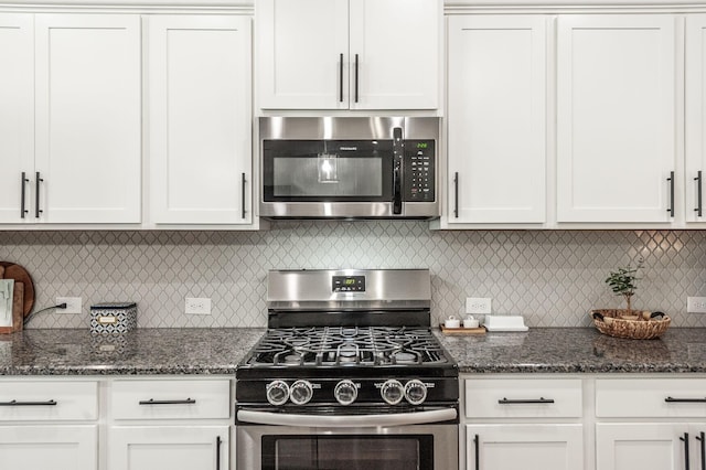 kitchen featuring tasteful backsplash, white cabinets, stainless steel appliances, and dark stone counters