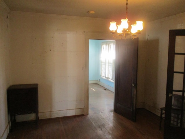 unfurnished room featuring a chandelier, wood finished floors, baseboards, and ornamental molding