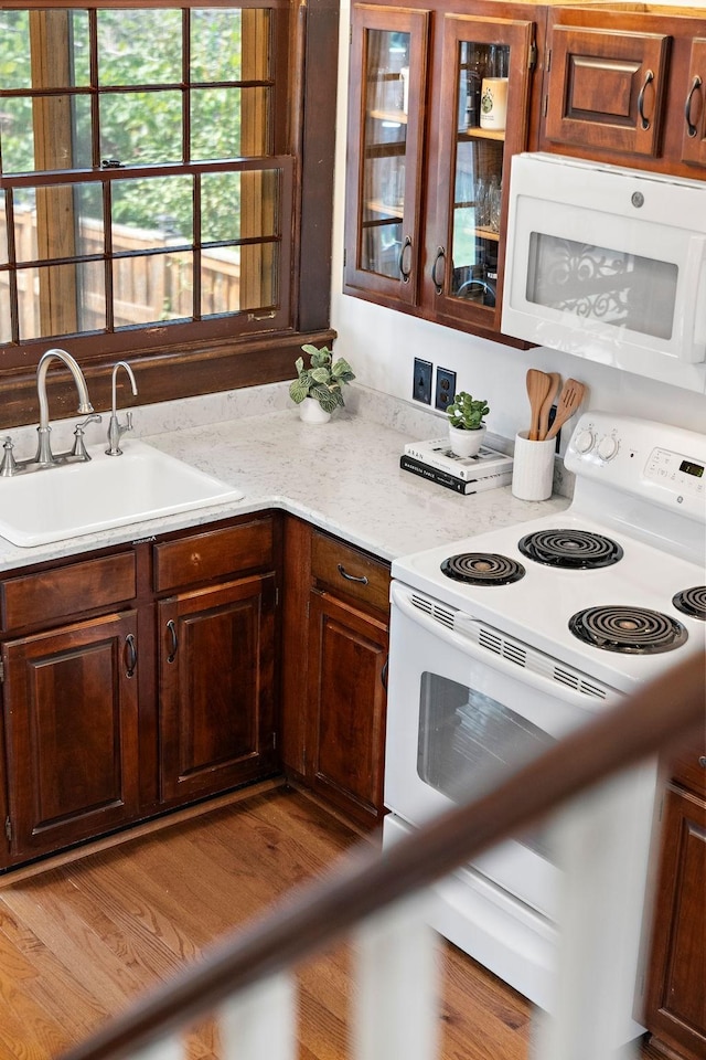 kitchen with glass insert cabinets, light stone counters, wood finished floors, white appliances, and a sink