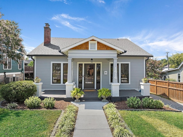 bungalow-style home with a shingled roof, a front lawn, fence, a porch, and a chimney