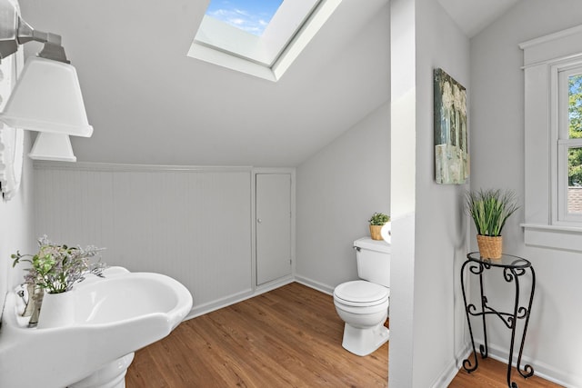 bathroom with lofted ceiling with skylight, toilet, and wood finished floors