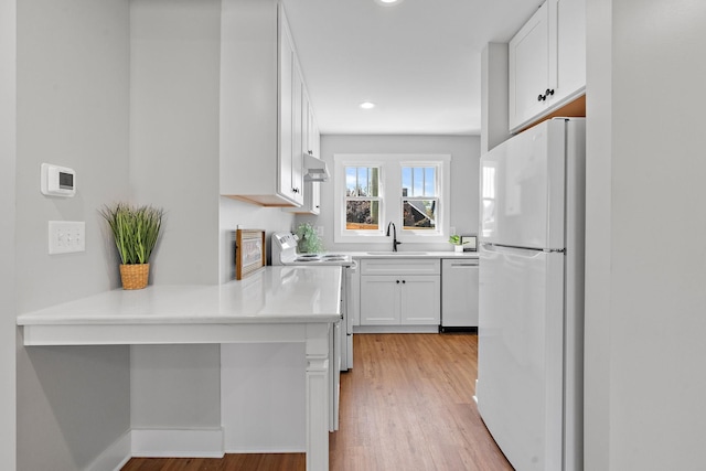 kitchen featuring light wood-type flooring, light countertops, white appliances, white cabinetry, and a sink