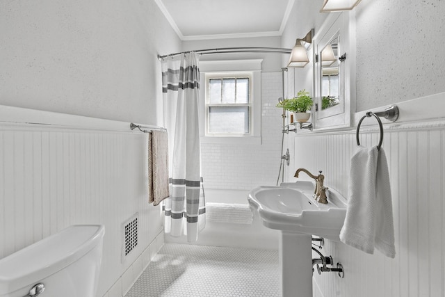 bathroom with a wainscoted wall, shower / bath combo, crown molding, toilet, and tile patterned floors