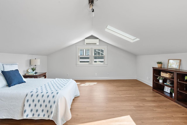 bedroom featuring baseboards, vaulted ceiling with skylight, a wall mounted air conditioner, and light wood-style floors