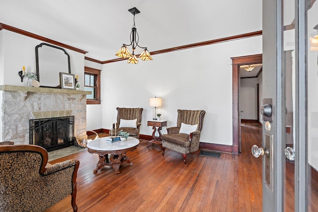 living area with baseboards, a fireplace with flush hearth, ornamental molding, hardwood / wood-style floors, and a notable chandelier