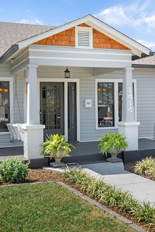 view of exterior entry with covered porch and a shingled roof