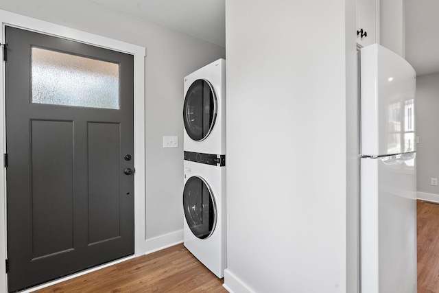 laundry room with laundry area, stacked washer / drying machine, baseboards, and wood finished floors