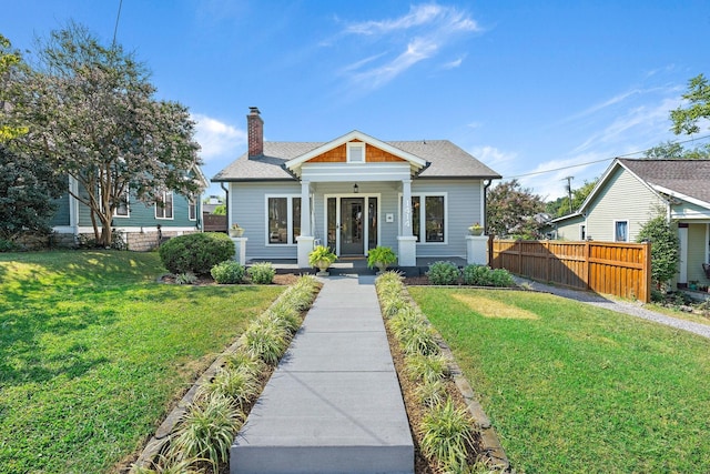 bungalow with a chimney, a shingled roof, a front lawn, and fence