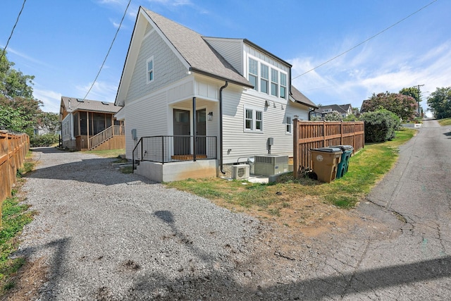 rear view of property featuring a shingled roof, fence, central AC, a sunroom, and driveway