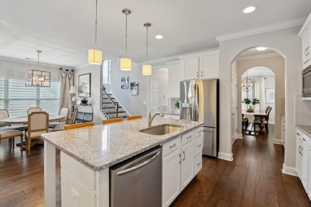 kitchen with dark wood-type flooring, ornamental molding, a center island with sink, a sink, and appliances with stainless steel finishes