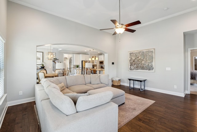 living area with dark wood finished floors, ceiling fan with notable chandelier, arched walkways, and baseboards