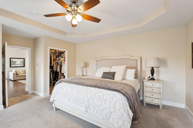 bedroom featuring a walk in closet, baseboards, carpet floors, a closet, and a raised ceiling