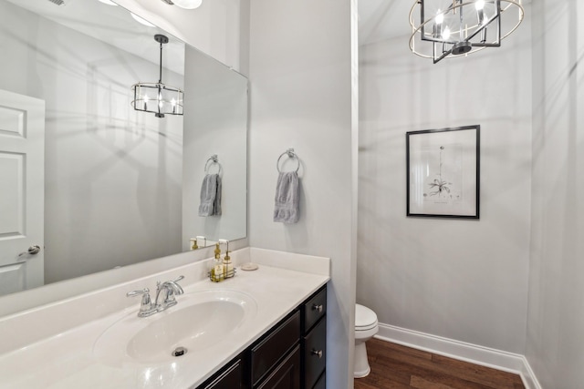 bathroom featuring baseboards, toilet, an inviting chandelier, wood finished floors, and vanity