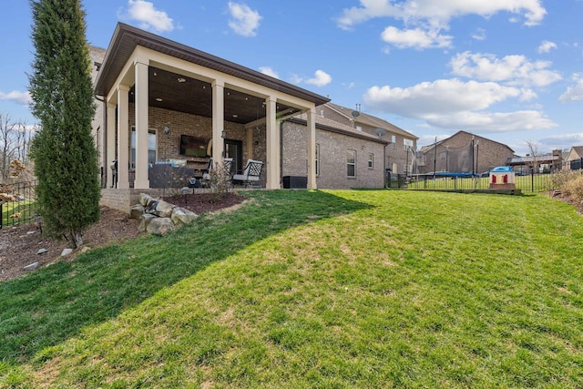 back of house with fence, a yard, a trampoline, a patio area, and brick siding