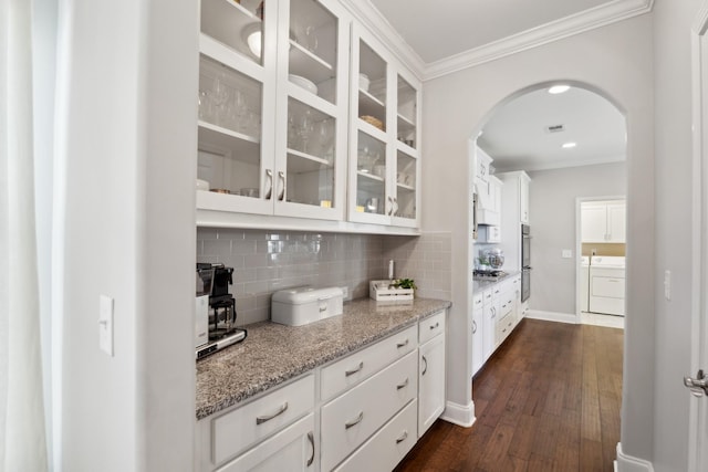 kitchen featuring glass insert cabinets, arched walkways, backsplash, and ornamental molding