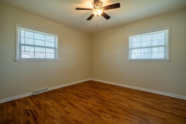 empty room with dark wood finished floors, visible vents, ceiling fan, and baseboards