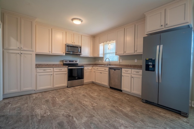 kitchen featuring a sink, appliances with stainless steel finishes, dark stone countertops, and white cabinetry