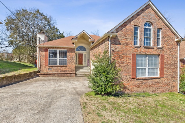 view of front facade featuring a front yard, brick siding, concrete driveway, and a chimney