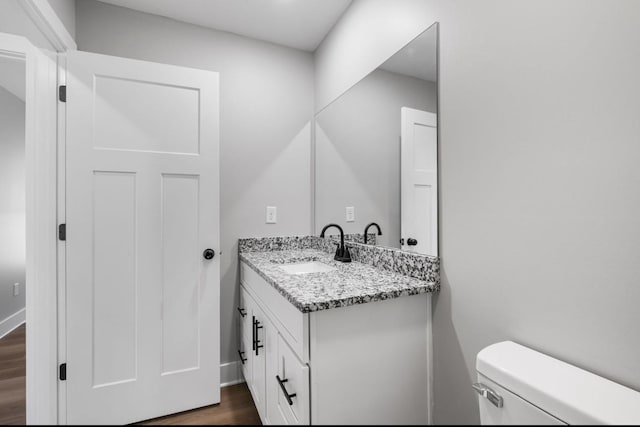 half bath featuring toilet, vanity, baseboards, and wood finished floors