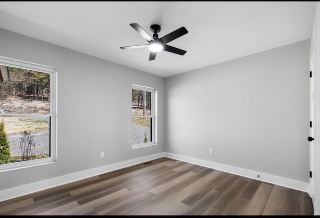 unfurnished room with dark wood-style floors, visible vents, ceiling fan, and baseboards