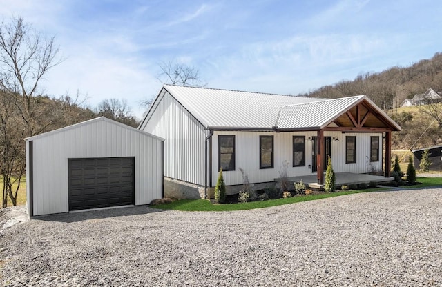 modern farmhouse with metal roof, gravel driveway, covered porch, and an outdoor structure