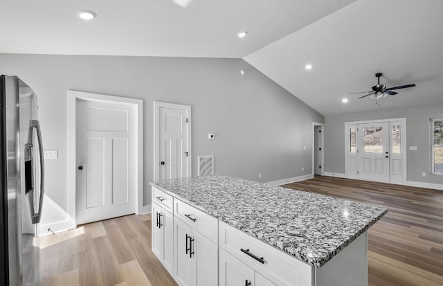 kitchen with light stone countertops, vaulted ceiling, stainless steel refrigerator with ice dispenser, light wood-type flooring, and a center island