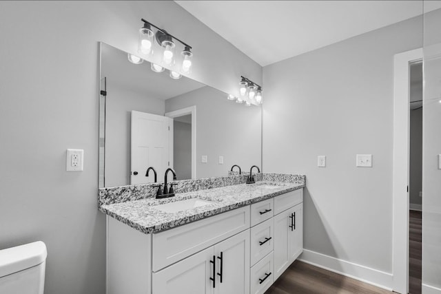 bathroom with a sink, baseboards, toilet, and double vanity