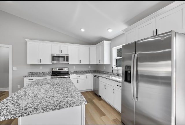 kitchen with a sink, a kitchen island, white cabinetry, appliances with stainless steel finishes, and lofted ceiling