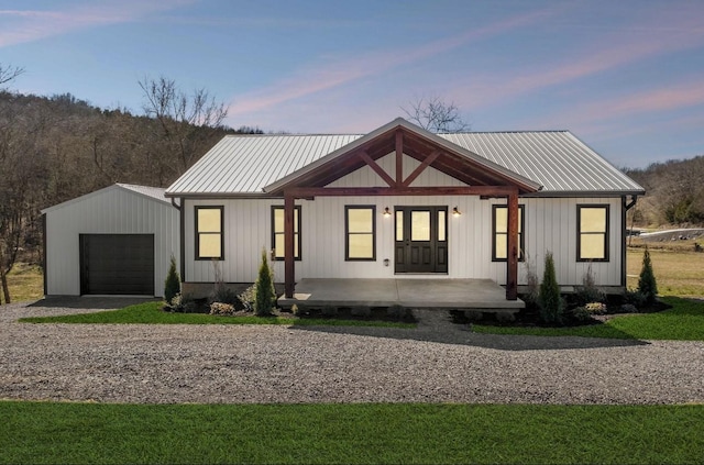 modern inspired farmhouse with driveway, board and batten siding, covered porch, an attached garage, and metal roof