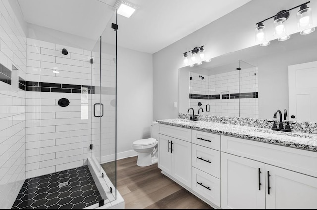 bathroom with double vanity, a stall shower, wood finished floors, and a sink