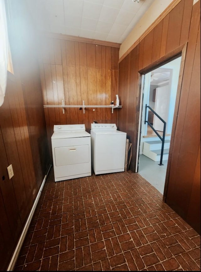 clothes washing area with washer and dryer, wooden walls, brick floor, and laundry area