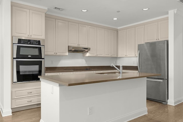 kitchen featuring light wood-type flooring, visible vents, under cabinet range hood, a sink, and stainless steel appliances