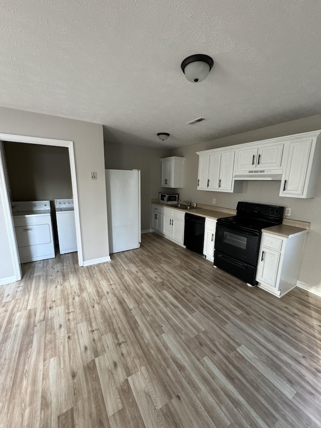 kitchen featuring light wood finished floors, visible vents, under cabinet range hood, washing machine and dryer, and black appliances