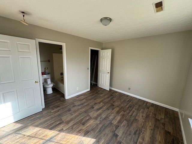 unfurnished bedroom featuring dark wood finished floors, ensuite bath, baseboards, and visible vents