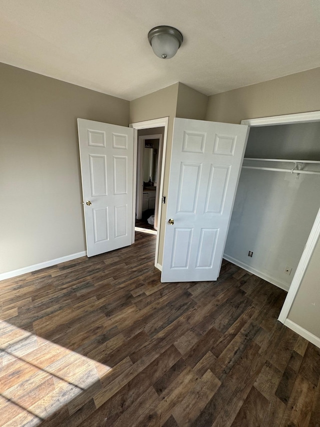 unfurnished bedroom with dark wood finished floors, baseboards, and a closet