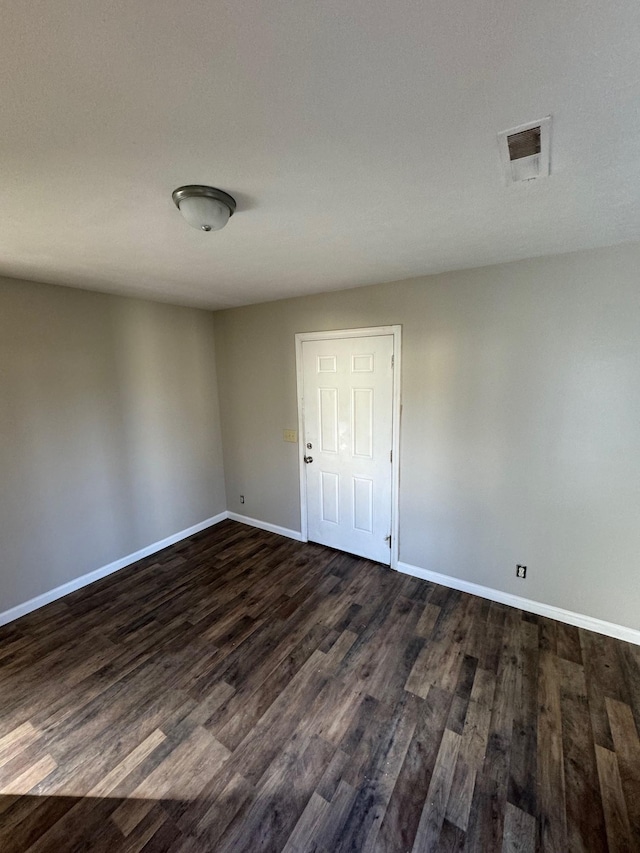 spare room with visible vents, baseboards, and dark wood-style floors