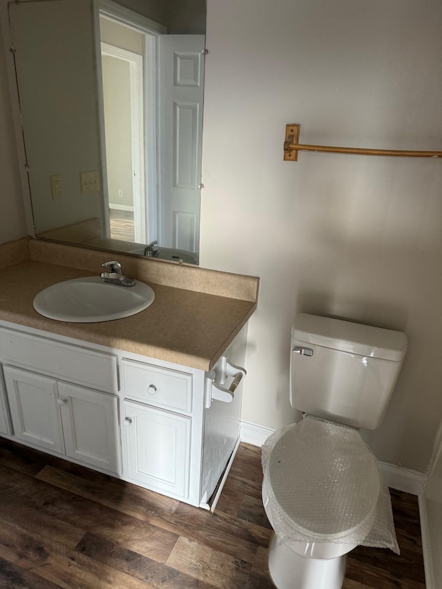 half bath featuring vanity, toilet, wood finished floors, and baseboards