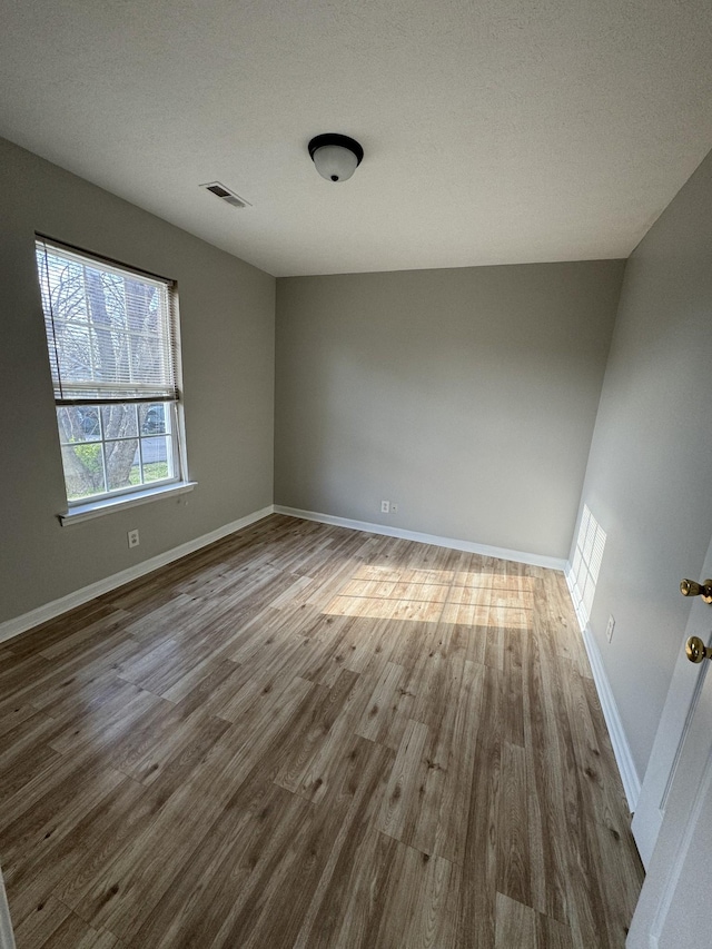 unfurnished room with visible vents, wood finished floors, baseboards, and a textured ceiling