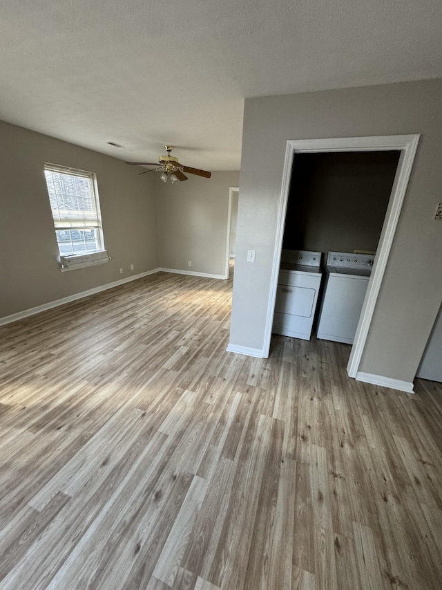 interior space with a ceiling fan, wood finished floors, baseboards, washing machine and clothes dryer, and a textured ceiling